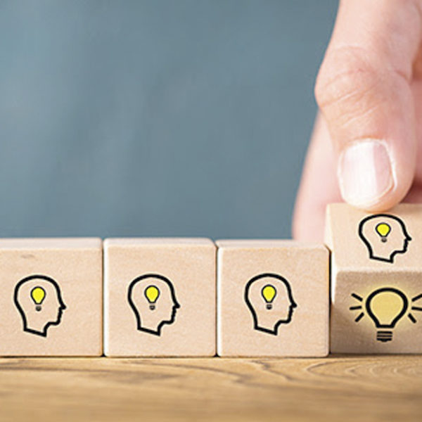 Four wooden cubes, three have a face with a lightbulb and one is being turned to the light bulb image.